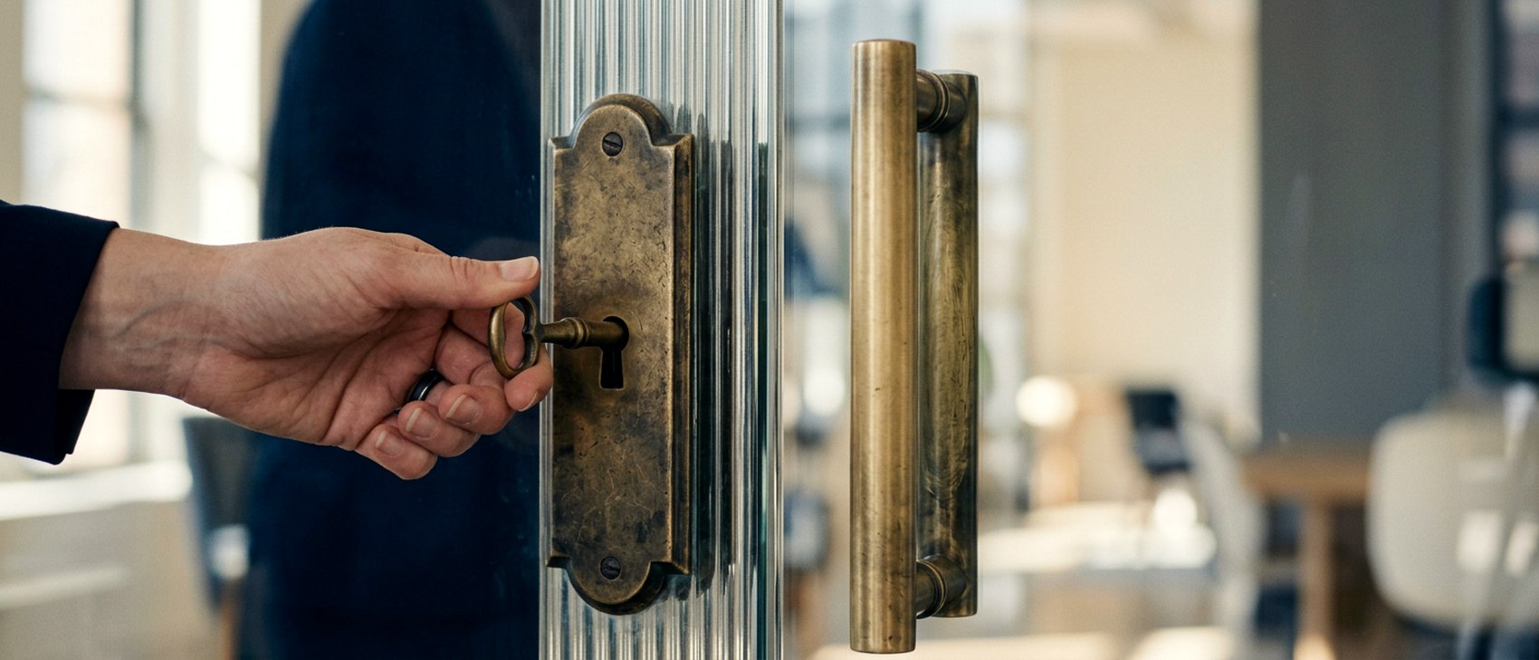 A hand turning a large aged brass key in the lock of an office door